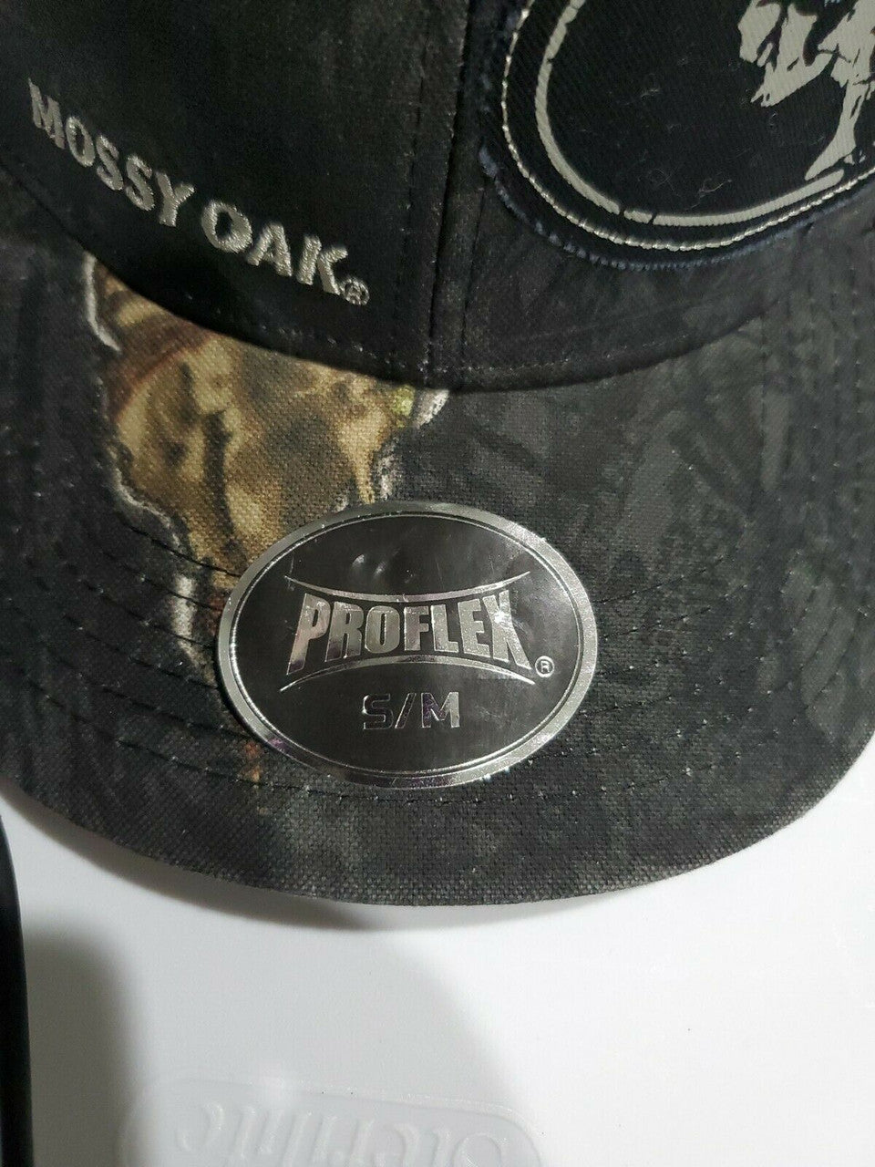 Mossy Oak men’s black camo stretch-fit hat in size S/M with logo patch and breathable mesh back, shown from multiple angles.