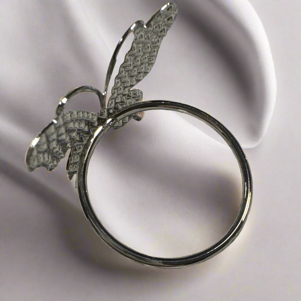 Set of 6 silver butterfly napkin rings displayed on cloth napkin and dish.