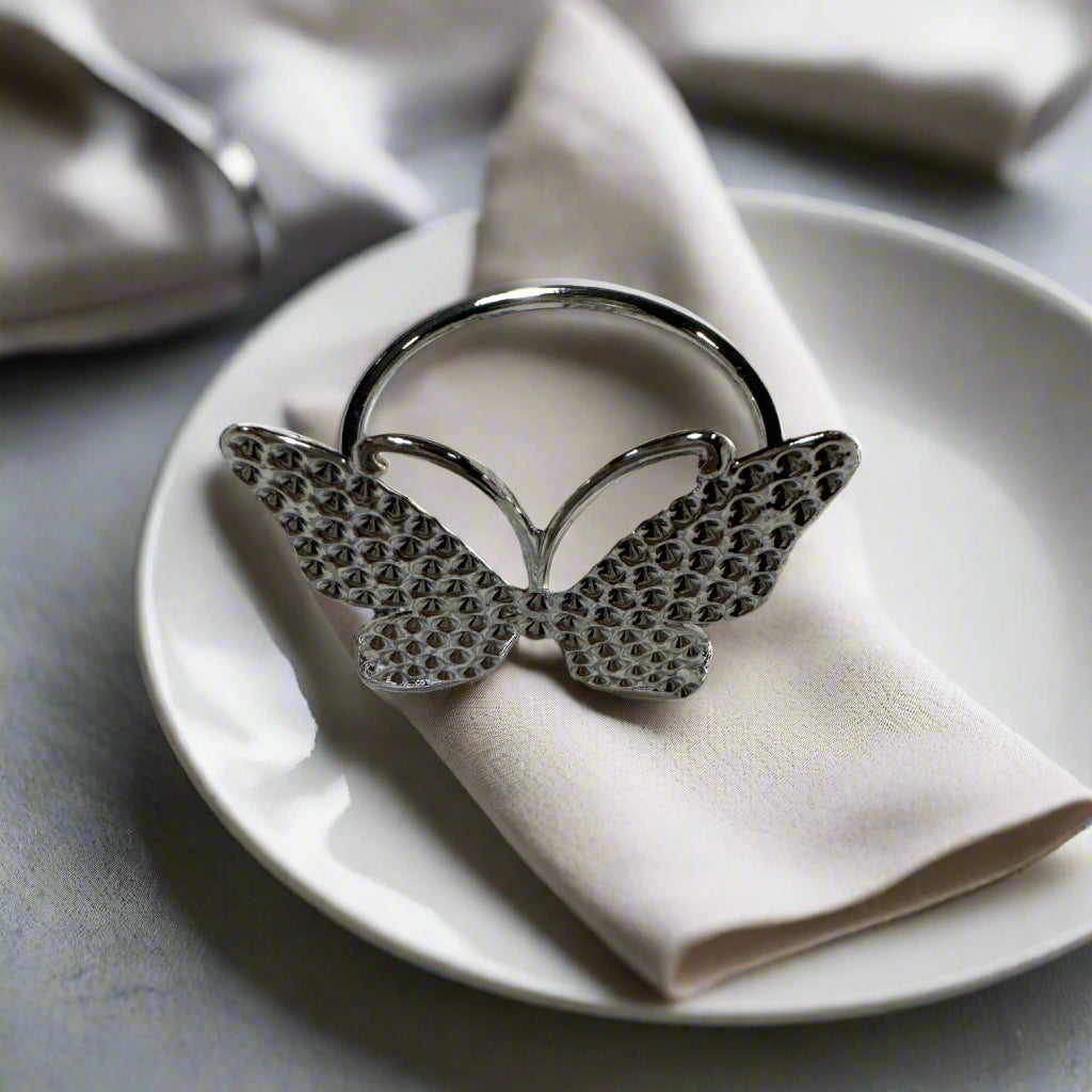 Set of 6 silver butterfly napkin rings displayed on cloth napkin and dish.