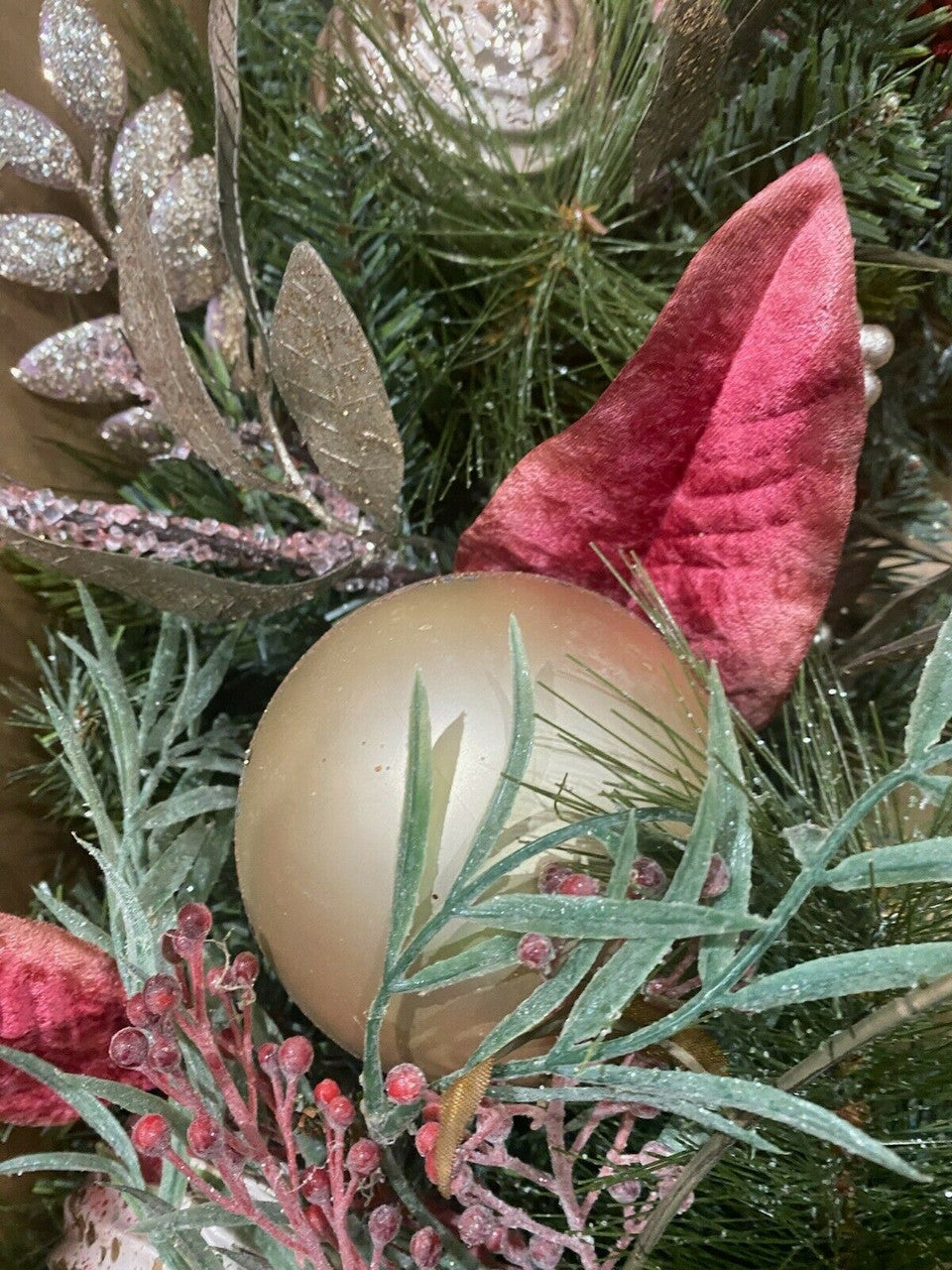 Gold ornament on a Christmas tree with green and red decorations.