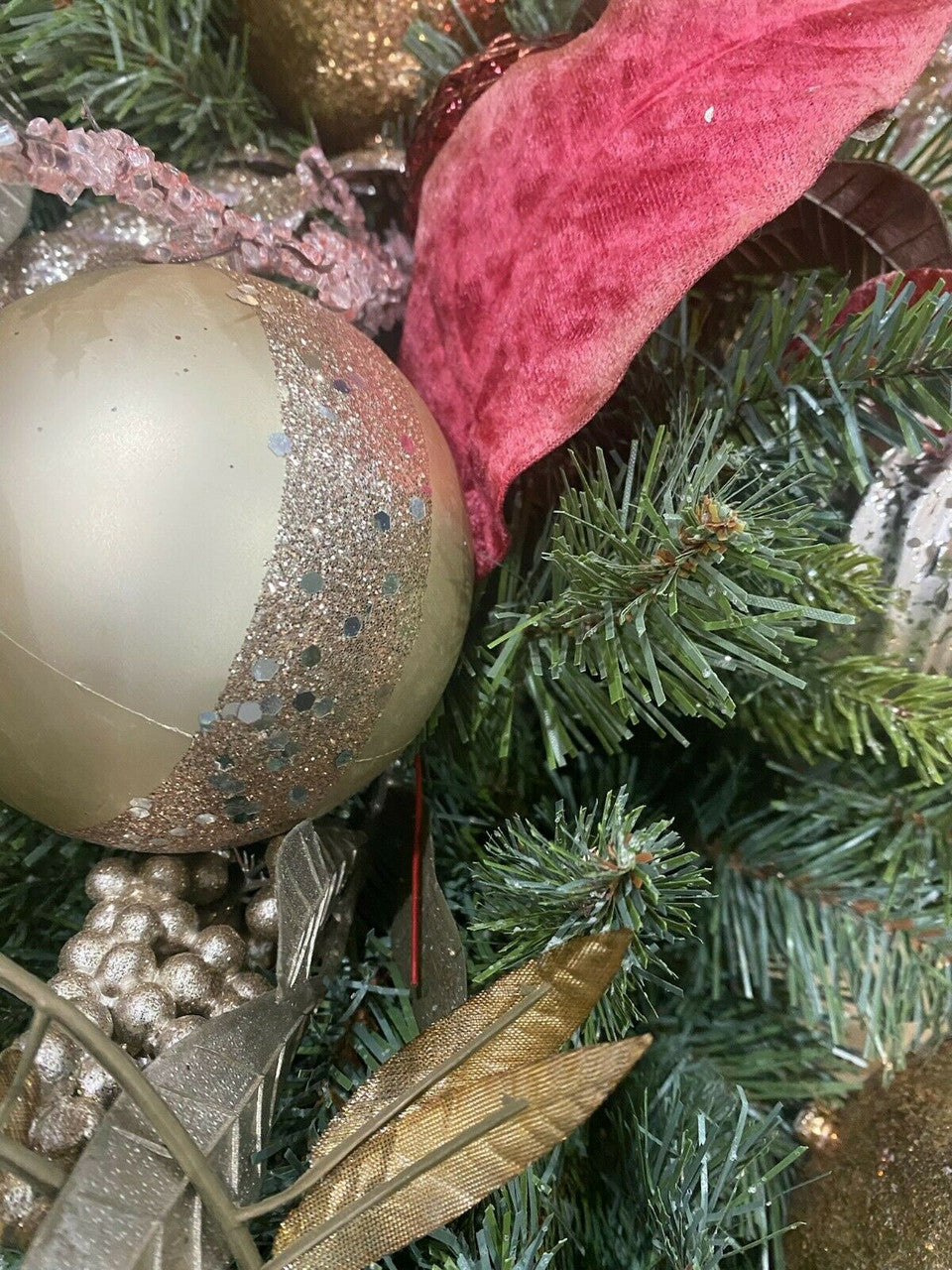 Close-up of Christmas tree decorations including a gold ball and red bow.