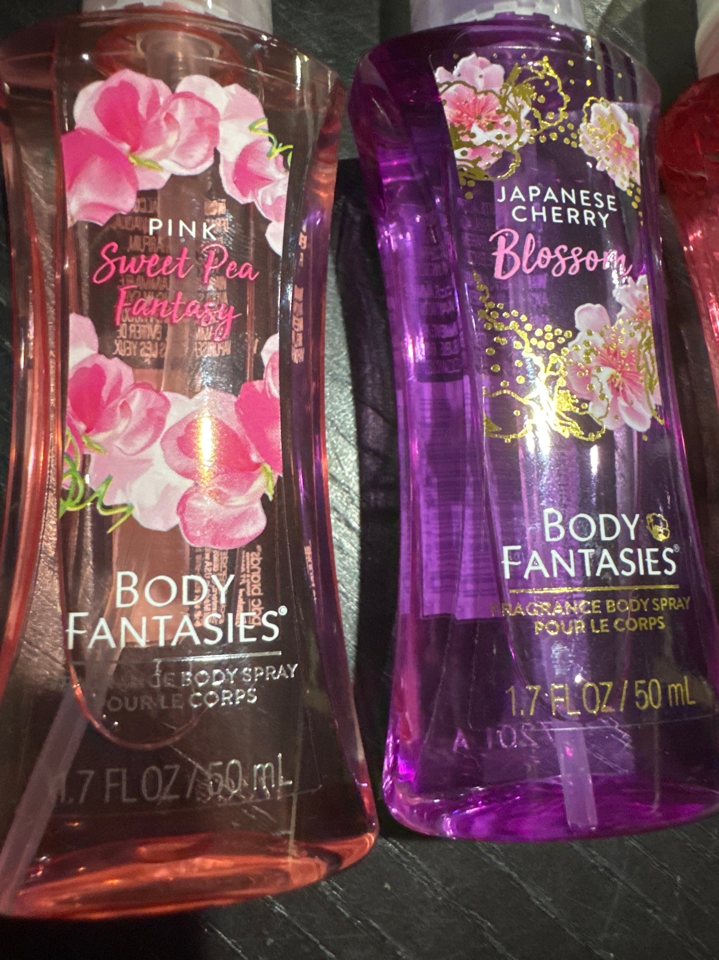 Two bottles of Body Fantasies scented products on a dark surface.